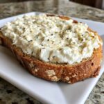 A thick slice of toasted bread generously topped with creamy cottage cheese toast and sprinkled with black pepper and herbs.