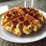A single, golden-brown cottage cheese waffle low carb served on a white plate against a granite countertop.