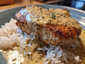 Close-up of a perfectly seared cajun chicken breast topped with creamy herb sauce, served on a bed of white rice.