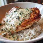 Close-up of a perfectly seared cajun chicken breast topped with creamy herb sauce, served over white rice in a bowl.