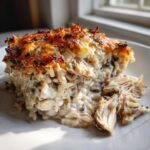 A close-up serving of creamy chicken wild rice casserole with a golden brown, crispy cheese topping.