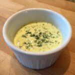 A small white ramekin filled with creamy, pale yellow salmon wellington sauce, topped with fresh dill.