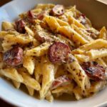 Close-up of creamy kielbasa pasta featuring penne noodles, sliced smoked sausage, and herbs.