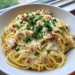 A close-up of creamy monterey chicken spaghetti topped with melted cheese, bacon bits, and fresh parsley.