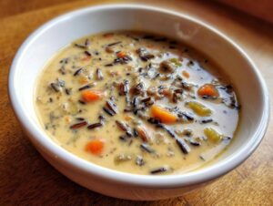Close-up of a creamy, thick wild rice soup featuring dark wild rice grains and chunks of orange carrots in a white bowl.