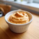 Close-up of a creamy, orange-colored dip for sweet potato fries in a small white ramekin.