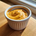Close-up of a creamy, orange-hued sweet potato fries dipping sauce in a white ramekin.