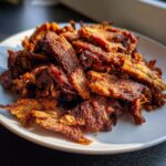 A close-up shot of crispy, browned homemade doner kebab meat piled high on a white plate.
