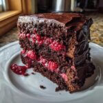 A decadent slice of dark chocolate raspberry cake layered with bright red raspberries and rich chocolate frosting.