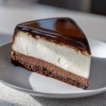 A perfect slice of Dubai chocolate cheesecake featuring layers of dark crust, chocolate mousse, white filling, and a glossy chocolate glaze.