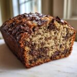 A close-up of a freshly baked loaf of gluten free chocolate chip banana bread, showing a moist crumb and melted chocolate chips on top.