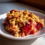 A close-up serving of bright red gluten free rhubarb crisp topped with golden, buttery crumble.