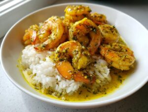 Close-up of vibrant Hawaiian garlic shrimp coated in a yellow, herby sauce served over white rice in a white bowl.