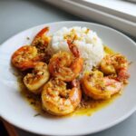 Six succulent pieces of Hawaiian garlic shrimp served with a mound of white rice on a white plate.