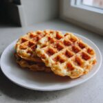 A stack of three golden-brown cottage cheese waffles served on a white plate near a window.
