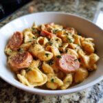 Close-up of creamy one pot kielbasa pasta with sliced sausage and parsley garnish in a white bowl.