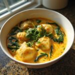 A close-up of quick coconut curry soup with dumplings, spinach, and fresh cilantro garnish.