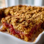 Close-up of a serving of rhubarb crisp with crumble topping showing the juicy red rhubarb filling.