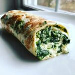A close-up, tasty shot of a spinach cottage cheese wrap cut open to show the creamy filling.