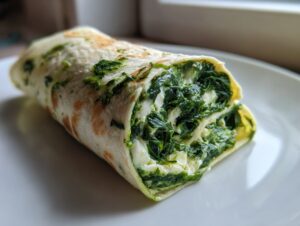 A delicious spinach cottage cheese wrap cut in half, showing the creamy white cottage cheese and dark green spinach filling.