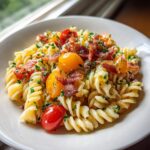 Close-up of a bowl of tangy tomato BLT pasta salad featuring fusilli pasta, cherry tomatoes, and crispy bacon bits.