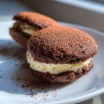 Two rich, dark chocolate tiramisu cookie crk sandwiches filled with creamy mascarpone filling and dusted heavily with cocoa powder.
