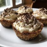 Four individual tiramisu cookie cups filled with cream and topped with chocolate shavings, sitting on a white plate.