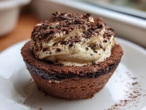 A single, decadent tiramisu cookie cup topped with piped mascarpone cream and dusted with cocoa powder.