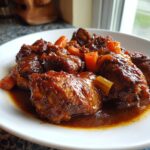 Close-up of rich, dark Trinidad brown stew chicken pieces served in a white bowl with carrots.