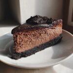 A perfect slice of ultimate chocolate cheesecake featuring a dark crust and rich mousse texture, topped with chocolate cookie crumbs.