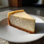 A thick, creamy slice of white chocolate cheesecake with a graham cracker crust on a white plate.