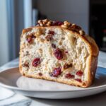 Cross-section of soft yeast bread with inclusions like dried cranberries and walnuts, served on a plate.
