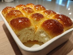 A close-up of freshly baked, glossy, fluffy dinner rolls nestled in a white baking dish.