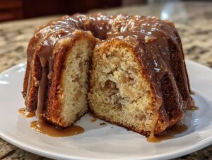 A bundt-style apple amaretto cake cut in half, showing moist interior and dripping with a thick caramel glaze.