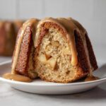 A slice of moist apple amaretto cake filled with visible apple chunks, topped with a thick caramel sauce drizzle.