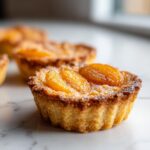 A close-up of one perfectly baked apricot-almond tartlet topped with glazed apricot halves on a marble surface.