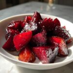 Close-up of glossy, deep red balsamic honey roasted beets chunks served in a small white bowl.