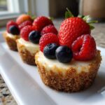 A close-up of delicious mini cheesecakes topped with fresh strawberries, raspberries, and blueberries on a white plate.