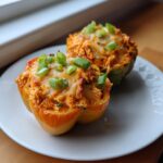 Two delicious buffalo chicken stuffed peppers, topped with melted cheese and fresh green onions, served on a white plate.