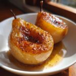 Two beautifully caramelized baked pears recipe halves sitting in syrup in a white bowl.