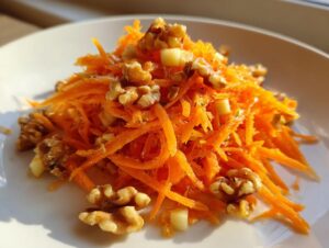 A bright, close-up view of a fresh carrot apple walnut salad piled on a white plate.