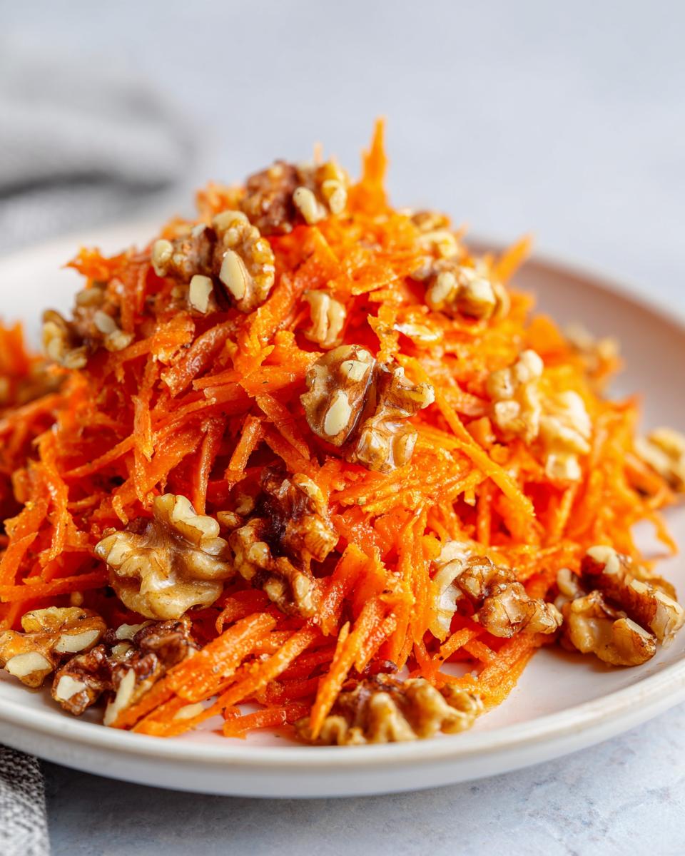 Close-up of a vibrant carrot apple walnut salad featuring shredded carrots topped generously with crunchy walnuts.