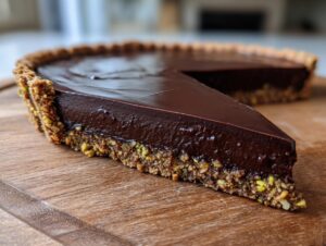 A close-up shot of a slice of chocolate pistachio tart showing the rich dark chocolate filling and textured pistachio crust.