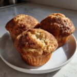 Three freshly baked greek yogurt apple muffins topped with cinnamon sugar on a white plate.