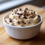 A close-up of creamy, peanut butter-based buckeye dip mixed generously with mini chocolate chips in a white bowl.