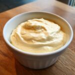 A close-up of thick, creamy homemade mayonnaise recipe eggless served in a small white ramekin on a wooden surface.