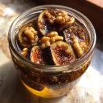 Close-up view of cut fresh figs and whole walnuts submerged in a rich liquid for fermented figs and walnuts in a small glass jar.