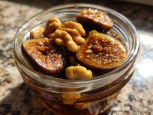 Close-up of halved, glistening fermented figs and walnuts soaking in liquid inside a small glass jar.