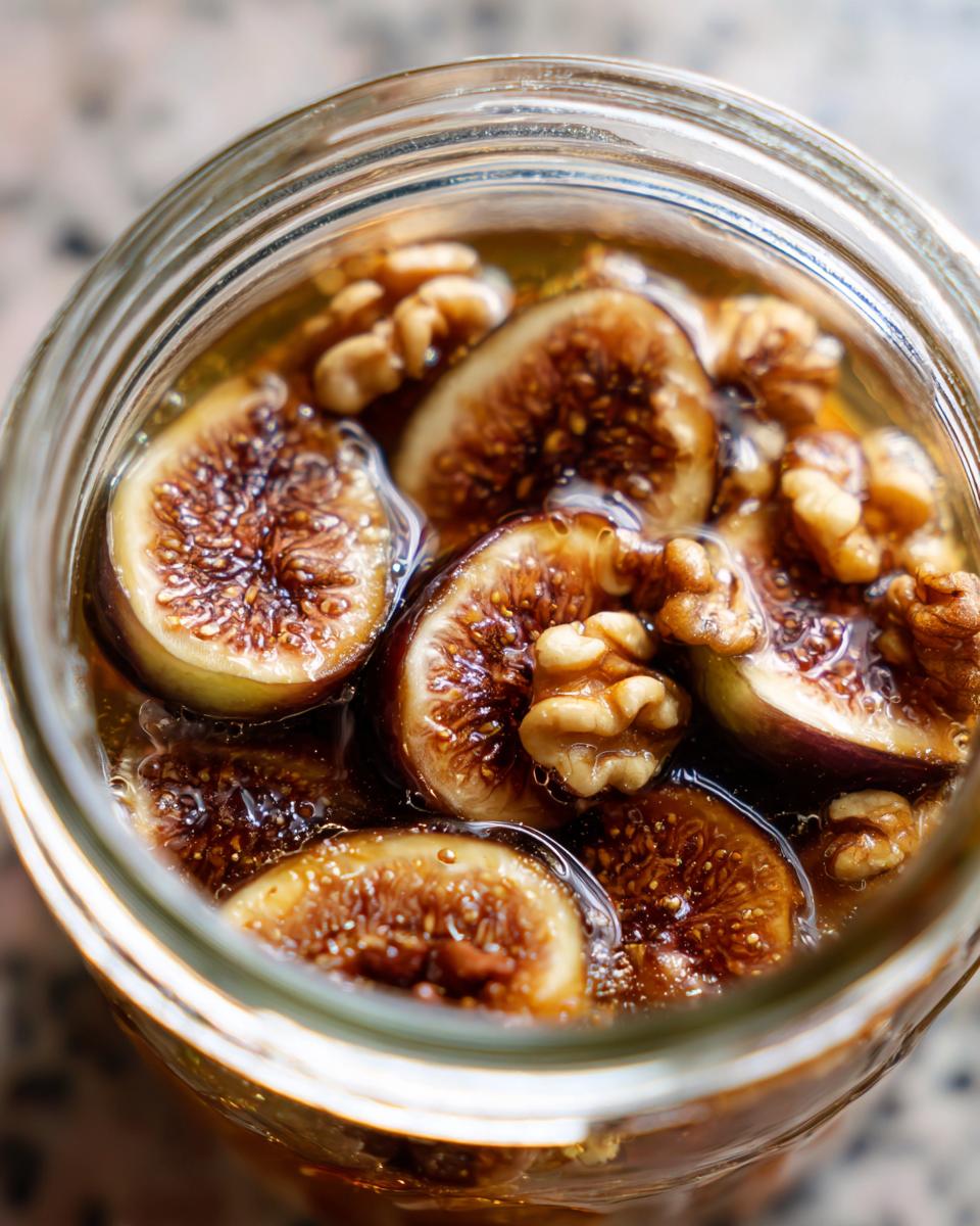 Close-up overhead view of sliced figs and walnuts submerged in liquid inside a glass jar for fermented figs and walnuts.