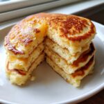 A tall stack of fluffy buttermilk pancakes cut to show the airy interior texture.